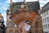 Flyer des MarburgPasses werden hochgehalten. Dahinter ist das Marburger Rathaus zu sehen.&nbsp;&copy;&nbsp;Stefanie Ingwersen, Stadt Marburg